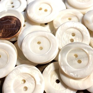May include: A pile of white, round, two-hole shell buttons. The buttons are approximately the size of a US penny.