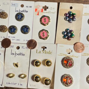 May include: A collection of vintage buttons on their original cards. The buttons vary in style, including gold, iridescent, and pearlized designs. Some cards feature the brand names "La Petite", "La Mode", and "Streamline".