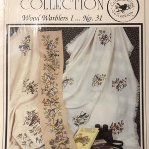 May include: A cross stitch pattern featuring a collection of wood warblers, a book titled "Warblers of the Americas", and a pair of binoculars. The pattern is titled "Wood Warblers I... No. 31" and is part of the "Crossed Wing Collection".