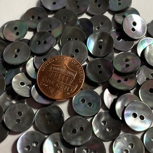 May include: A pile of black and iridescent shell buttons with two holes each. A US penny is included for scale.
