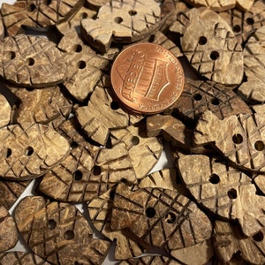 May include: A pile of brown coconut shell buttons in the shape of a fish. The buttons have two holes each and are approximately the size of a US penny.
