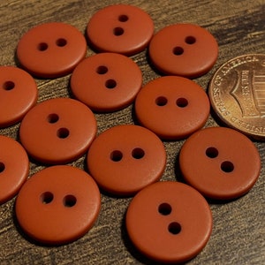 May include: Twelve brown plastic buttons with two holes each. The buttons are arranged in a circle around a penny.