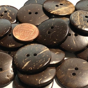 May include: A pile of brown coconut shell buttons with two holes each. A US penny is placed on top of the buttons for scale.