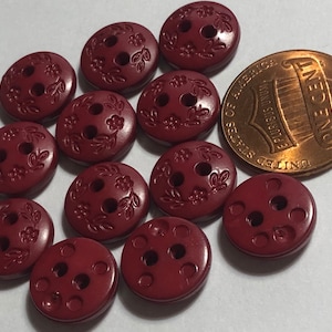 May include: Twelve burgundy two-hole buttons with a floral design. The buttons are approximately the size of a US penny.
