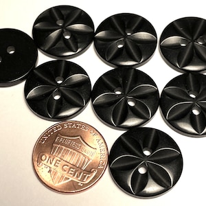 May include: Eight black plastic buttons with a flower design. The buttons have two holes each and are approximately the size of a US penny.