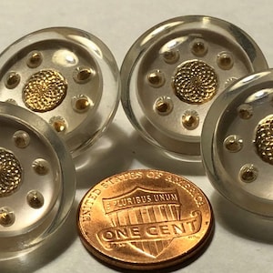 May include: Four clear glass buttons with a gold center design and silver accents. The buttons are approximately the size of a US penny.
