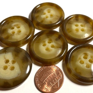 May include: Six brown and cream-colored buttons with four holes each. The buttons have a marbled appearance and are arranged on a white surface. A US one-cent coin is included for size reference.