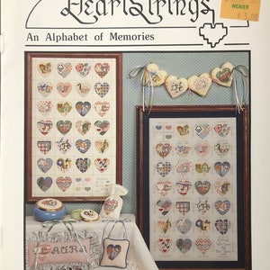May include: A cross-stitch pattern booklet titled "HeartStrings: An Alphabet of Memories" by Pat Thode, featuring a colorful alphabet of hearts with various designs. The booklet includes a sample of the finished cross-stitch project.