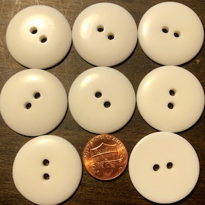 May include: Nine white round buttons with two holes each. The buttons are arranged in a 3x3 grid. A penny is placed in the center of the grid for scale.