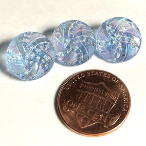 May include: Three iridescent blue glass buttons with a swirl design. The buttons are approximately the size of a US penny.
