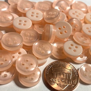 May include: A pile of 4-hole, translucent, peach-colored buttons. The buttons are about the size of a US penny.