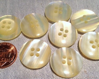 May include: Eight iridescent white and yellow buttons with four holes each. The buttons are approximately the size of a UK penny.