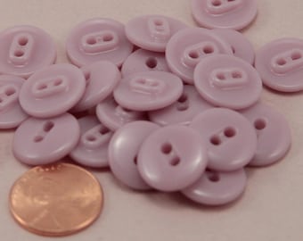 May include: A pile of light purple plastic buttons with two holes each. The buttons are about the size of a UK penny.
