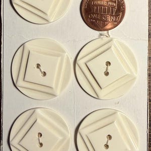 May include: Five off-white circular buttons with a raised square center and two holes, attached to a white card labeled SUPERIOR QUALITY. A copper-colored United States one-cent coin is placed next to the top left button for size reference.