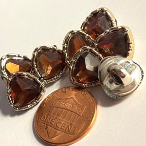 May include: Six brown heart-shaped buttons with silver trim and a single silver button with a loop on the back. The buttons are about the size of a US penny.