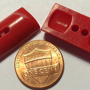 May include: Two red plastic buttons, one with a single hole and the other with two holes. The buttons are shown next to a US penny for scale.