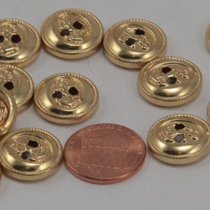 May include: A collection of 11 gold-colored buttons with two holes each. The buttons feature a raised design of an anchor and a rope border. The buttons are approximately the size of a US penny.