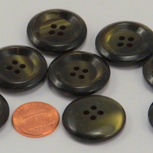 May include: Eight black and green four-hole buttons. The buttons are round and have a raised edge. They are approximately the size of a US penny.