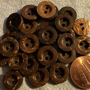 May include: A collection of 20 brown coconut shell buttons with two holes each. The buttons are arranged in a circle with a penny in the center.