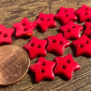 May include: A group of 12 red star-shaped buttons with two holes each. The buttons are about the size of a US penny.