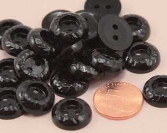 May include: A pile of black plastic buttons with two holes each. The buttons have a textured, slightly raised design. A US penny is included for scale.