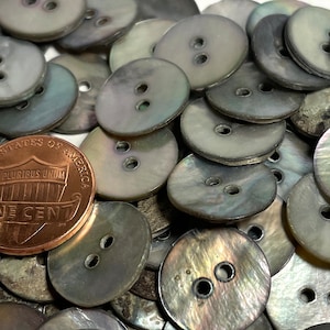 May include: A pile of iridescent gray mother of pearl buttons with two holes each. The buttons are oval shaped and have a smooth, shiny finish.