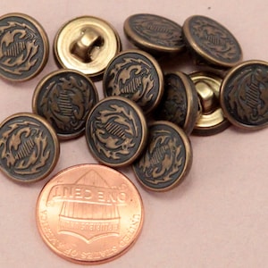 May include: A group of 10 bronze-colored buttons with a decorative design. The buttons have a shank back and are approximately the size of a US penny.