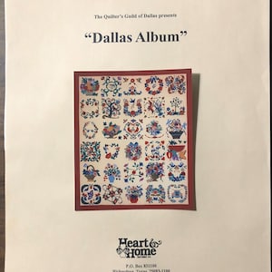 May include: A colorful quilt pattern with a variety of floral and geometric designs. The quilt is titled "Dallas Album" and is presented by The Quilter's Guild of Dallas. The quilt is printed on a white background with the text "Heart & Home Pattern Co. P.O. Box 831100 Richardson, Texas 75083-1100".
