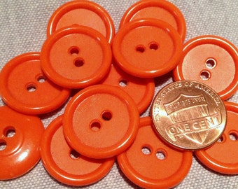 May include: A collection of ten orange plastic buttons, each with two holes. The buttons are arranged in a circle with a penny in the centre.