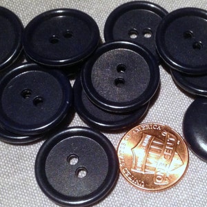 May include: A collection of ten dark blue plastic buttons with two holes each. The buttons are arranged in a circle with a penny in the center.