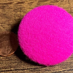 May include: A bright pink, round, fuzzy felt circle. The circle is about the size of a US penny.