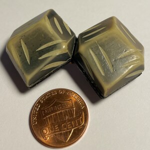 May include: Two beige and black geometric shaped buttons with a carved design. The buttons are about the size of a US penny.