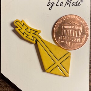 May include: A yellow plastic button with a black design. The button is shaped like a kite with a tail. The button is on a white card with the text "Dutton Crafts by La Mode" and the number "235".