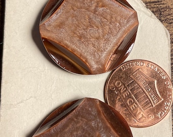 May include: Two vintage brown buttons with a diamond-shaped design, set on a vintage card with a penny for size comparison. The buttons have a glossy finish and a textured surface.
