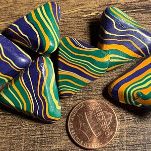 May include: Six triangular shaped polymer clay beads with a striped pattern in shades of green, yellow, and purple.