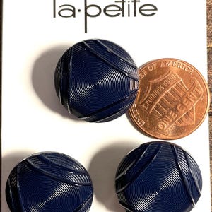May include: Three navy blue buttons with a spiral design, displayed on a white card with the text "la.petite". The card also includes the text "WASHABLE AND DRY CLEANABLE" and "Sz 3/4" (19MM)". A penny is next to the buttons.