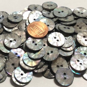 May include: A pile of gray iridescent shell buttons with a sunburst design and two holes. The buttons are approximately the size of a US penny.