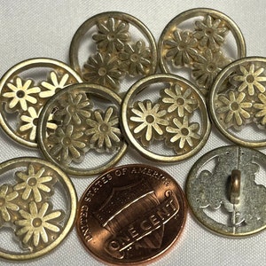 May include: Ten gold-toned metal buttons with a daisy design. Each button has a raised daisy design with three daisies in the center. The buttons are round and have a smooth, shiny finish.