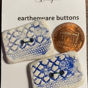 May include: Two white ceramic buttons with a blue and white pattern. The buttons are rectangular and have two holes. The buttons are machine washable. The Logger's Daughter logo is visible in the background.