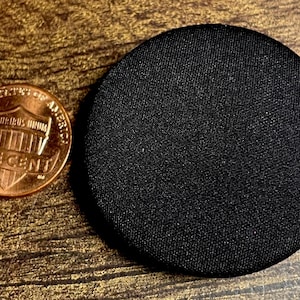 May include: A close-up shot of a copper one-cent coin next to a black, circular object. The coin displays the image of Abraham Lincoln and the words "ONE CENT". The black object has a textured surface.