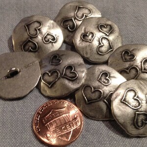 May include: A set of eight silver-toned metal buttons with a hammered finish. Each button features three raised heart designs.