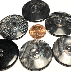 May include: Six black and silver buttons with a shiny finish. The buttons have a single or double hole in the center. One button is next to a US penny for size comparison.