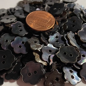 May include: A pile of black shell buttons in a flower shape with two holes. The buttons are about the size of a US penny.