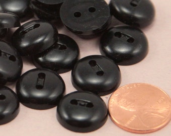 May include: A pile of black plastic buttons with two holes. The buttons are about the size of a US penny.