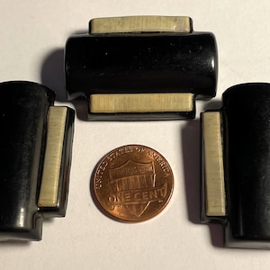 May include: Three black and white rectangular buttons with a rounded edge. The buttons have a black background and two white stripes on each side. The buttons are about the size of a US penny.