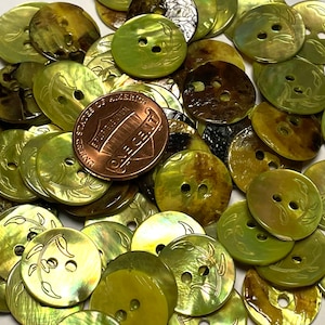 May include: A collection of green, brown, and gold shell buttons with a leaf design. The buttons are arranged in a pile and have two holes each.
