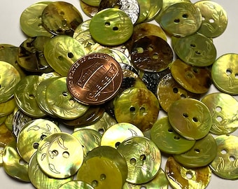 May include: A collection of green, brown, and gold shell buttons with a leaf design. The buttons are arranged in a pile and have two holes each.