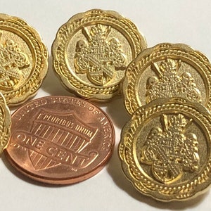 May include: Six gold-colored buttons with a raised design featuring a crest and a rope border. One button is plain with a loop on the back.