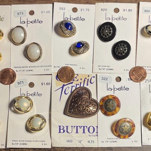 May include: Assortment of vintage buttons on cards, including gold, pearl, and jewel-toned designs. Various shapes and sizes are displayed, with some featuring the "la petite" brand. Some cards include the text "BUTTONS".