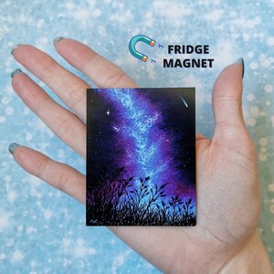 May include: A fridge magnet featuring a painting of a starry night sky with a blue and purple nebula, silhouetted by tall grass. The magnet is rectangular and has a glossy finish.